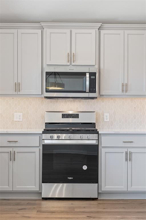 kitchen featuring white cabinets, appliances with stainless steel finishes, light hardwood / wood-style floors, and decorative backsplash