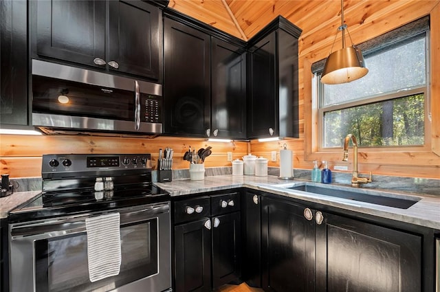 kitchen with appliances with stainless steel finishes, vaulted ceiling, sink, hanging light fixtures, and wood walls