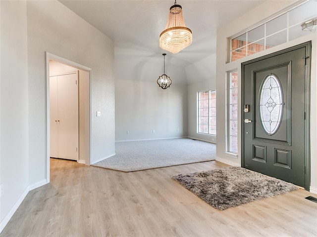 entrance foyer with vaulted ceiling, light hardwood / wood-style floors, and an inviting chandelier