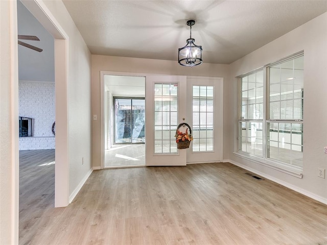 interior space featuring ceiling fan with notable chandelier, light hardwood / wood-style flooring, and a brick fireplace