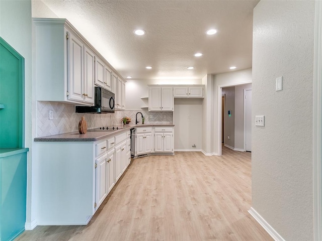 kitchen featuring white cabinets, black appliances, sink, decorative backsplash, and light wood-type flooring