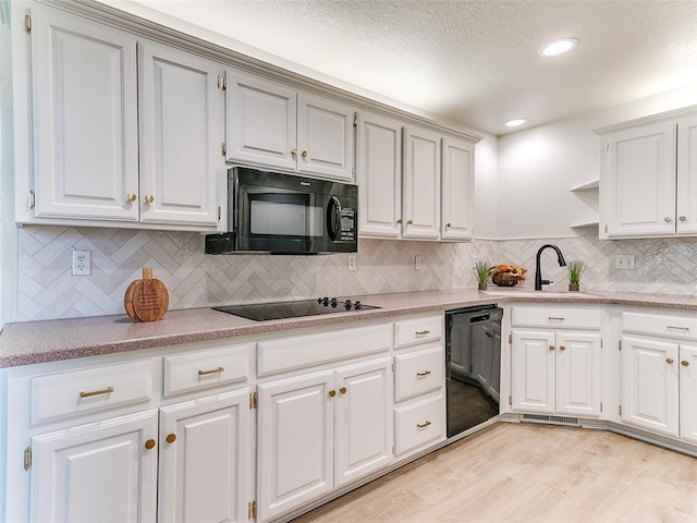 kitchen with decorative backsplash, white cabinets, black appliances, and light wood-type flooring