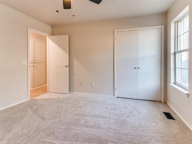 unfurnished bedroom featuring ceiling fan, light colored carpet, and a closet