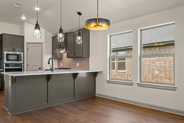 kitchen featuring a kitchen bar, hanging light fixtures, appliances with stainless steel finishes, dark hardwood / wood-style flooring, and kitchen peninsula