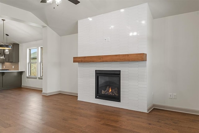 unfurnished living room featuring ceiling fan, a large fireplace, lofted ceiling, and dark wood-type flooring