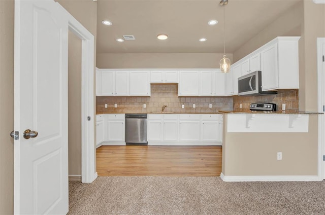 kitchen featuring appliances with stainless steel finishes, light hardwood / wood-style floors, white cabinetry, and pendant lighting