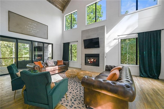 living room with a tiled fireplace, plenty of natural light, high vaulted ceiling, and wood-type flooring