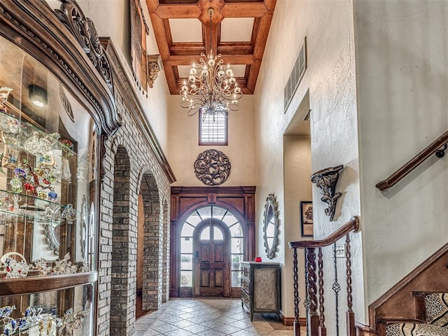 foyer entrance with a high ceiling, coffered ceiling, a notable chandelier, and beam ceiling