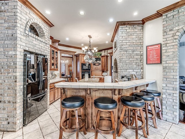 kitchen with tile counters, kitchen peninsula, crown molding, a chandelier, and black appliances