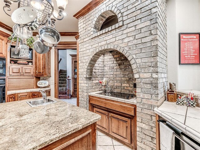 kitchen with ornamental molding, light tile patterned floors, black appliances, and sink