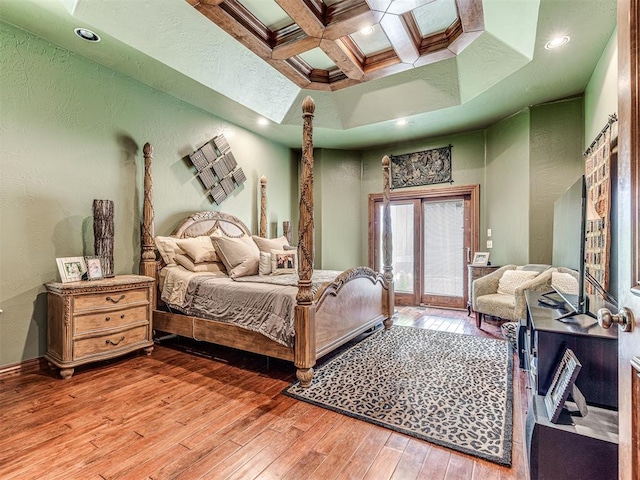 bedroom featuring hardwood / wood-style floors, decorative columns, coffered ceiling, and beam ceiling