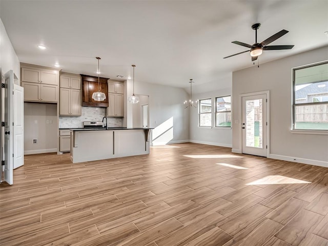 kitchen featuring pendant lighting, a center island with sink, ceiling fan with notable chandelier, decorative backsplash, and light wood-type flooring