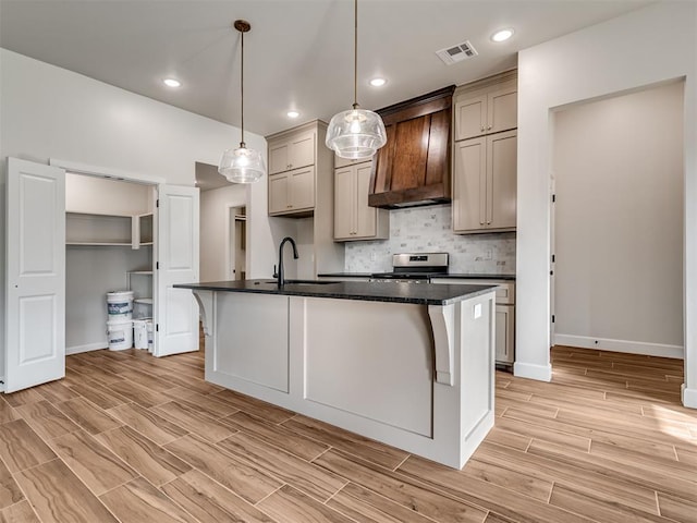 kitchen featuring sink, decorative light fixtures, a center island with sink, stainless steel stove, and custom range hood