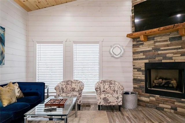 living room with hardwood / wood-style flooring, vaulted ceiling, wood walls, and a stone fireplace