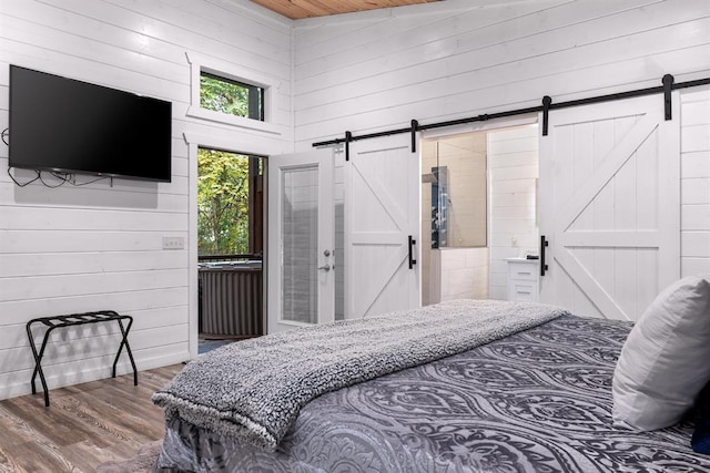 bedroom with hardwood / wood-style floors, multiple windows, wooden walls, and a barn door