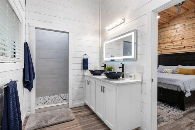 bathroom with hardwood / wood-style floors, lofted ceiling, vanity, wood walls, and tiled shower