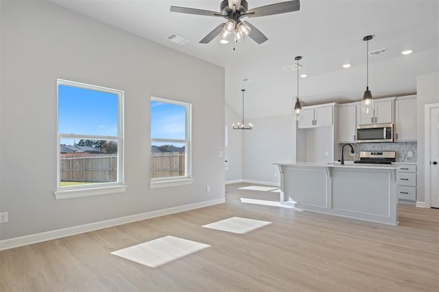 kitchen with stainless steel appliances, hanging light fixtures, a center island with sink, and light hardwood / wood-style floors