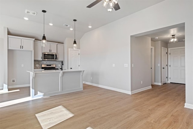 kitchen featuring appliances with stainless steel finishes, light wood-type flooring, ceiling fan, decorative light fixtures, and an island with sink