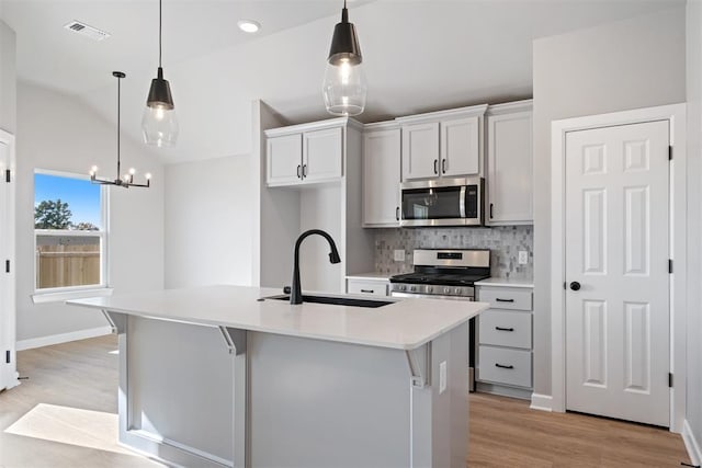 kitchen featuring stainless steel appliances, sink, decorative light fixtures, a center island with sink, and lofted ceiling