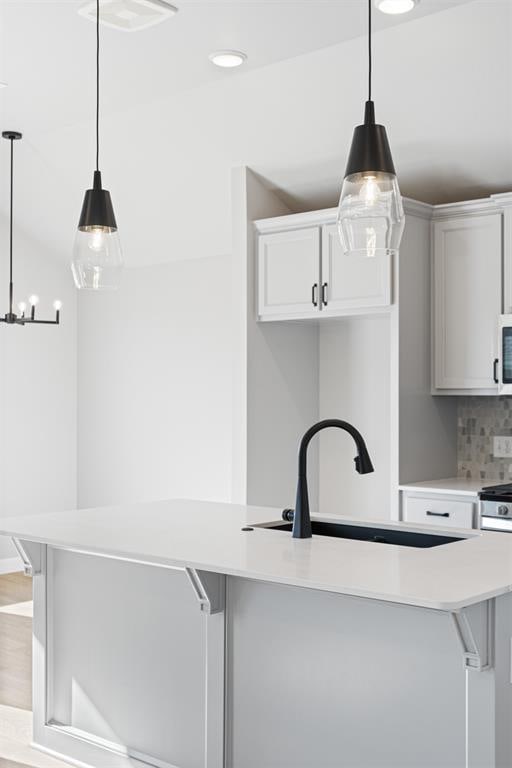 kitchen featuring decorative backsplash, light hardwood / wood-style flooring, hanging light fixtures, and an island with sink