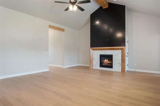 unfurnished living room with ceiling fan, beam ceiling, high vaulted ceiling, a premium fireplace, and light hardwood / wood-style floors