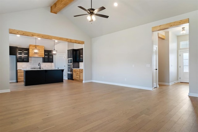 unfurnished living room featuring light wood-type flooring, ceiling fan, sink, high vaulted ceiling, and beamed ceiling