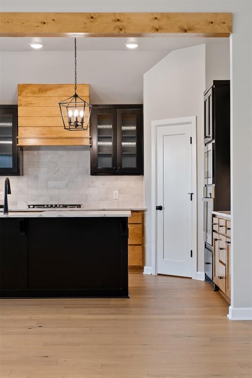 kitchen featuring stainless steel oven, light wood-type flooring, decorative light fixtures, and backsplash