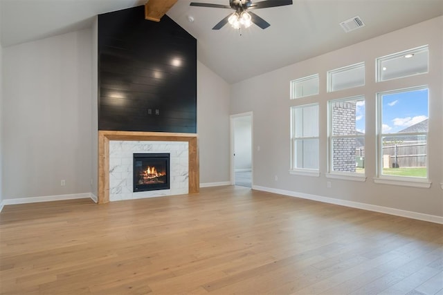 unfurnished living room featuring a high end fireplace, light hardwood / wood-style floors, ceiling fan, and beamed ceiling