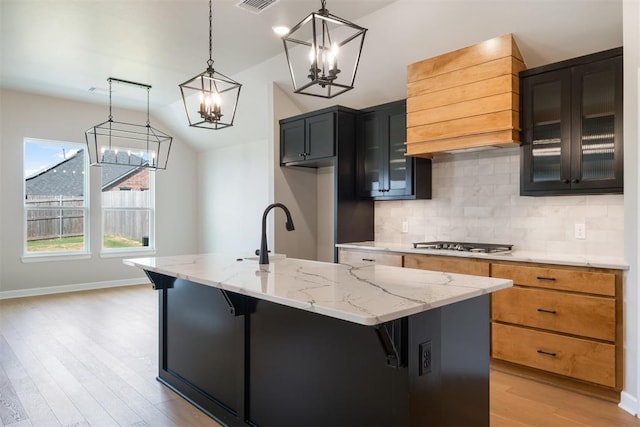 kitchen featuring lofted ceiling, a center island with sink, hanging light fixtures, light hardwood / wood-style flooring, and light stone countertops