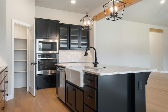 kitchen featuring sink, light hardwood / wood-style floors, decorative light fixtures, a kitchen island with sink, and appliances with stainless steel finishes