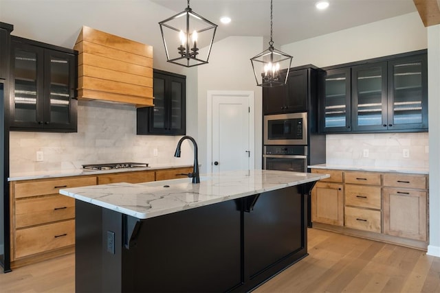 kitchen featuring appliances with stainless steel finishes, a kitchen island with sink, light brown cabinets, light hardwood / wood-style floors, and hanging light fixtures