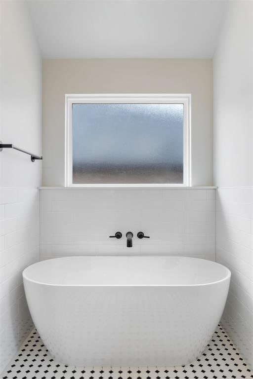 bathroom with tile patterned floors, a tub to relax in, and tile walls