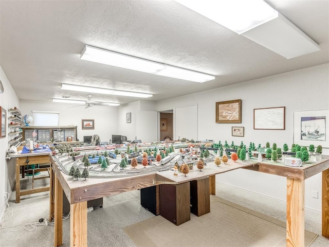 recreation room with a textured ceiling, light colored carpet, and ceiling fan