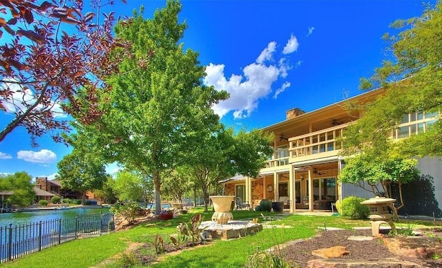 back of property with ceiling fan, a balcony, and a water view