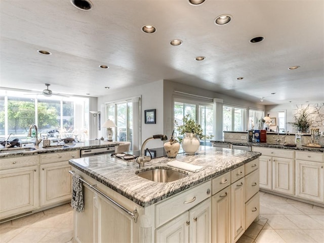 kitchen featuring stone countertops, sink, light tile patterned floors, and a kitchen island with sink