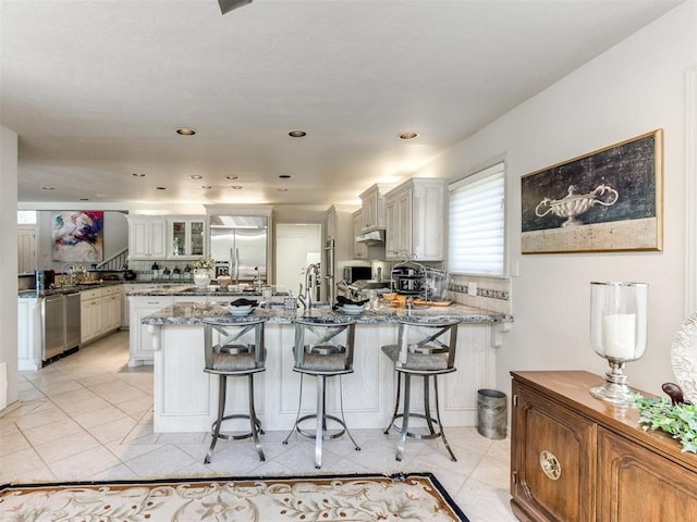 kitchen featuring stone counters, a breakfast bar area, decorative backsplash, kitchen peninsula, and stainless steel appliances