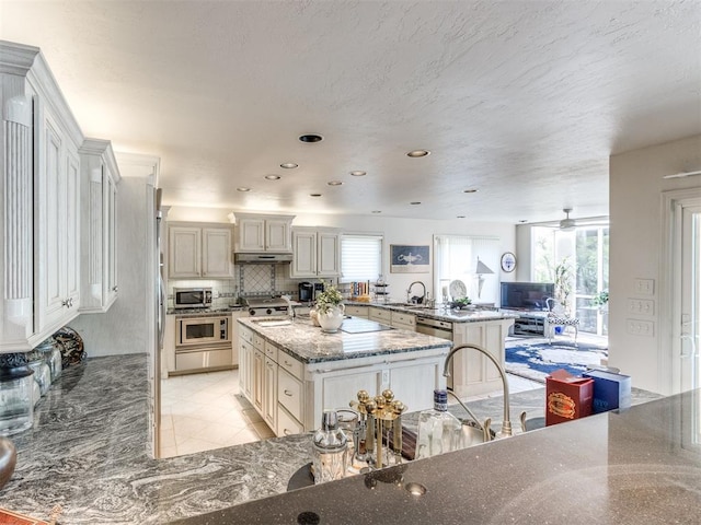 kitchen featuring stone counters, sink, ceiling fan, a kitchen island with sink, and a breakfast bar