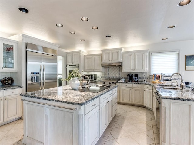 kitchen with appliances with stainless steel finishes, sink, light tile patterned floors, dark stone countertops, and an island with sink