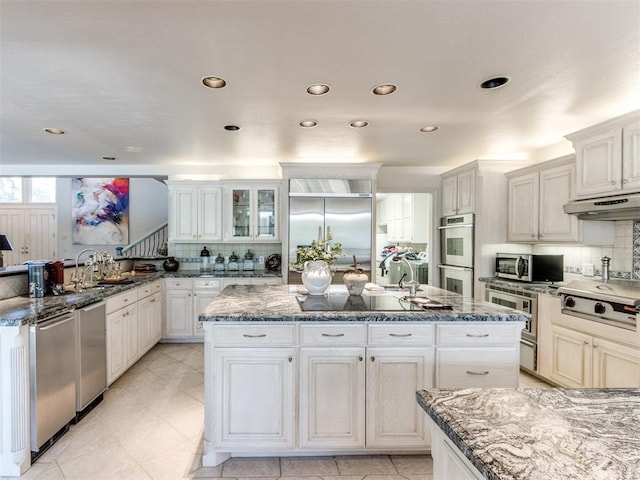 kitchen with a center island, built in appliances, dark stone countertops, tasteful backsplash, and white cabinetry