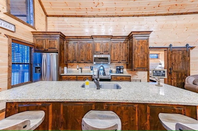 kitchen featuring appliances with stainless steel finishes, a kitchen island with sink, wooden walls, and a breakfast bar