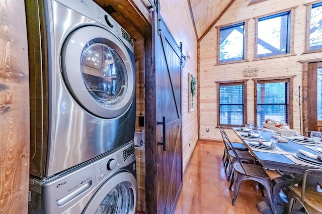 laundry room featuring stacked washing maching and dryer, a barn door, plenty of natural light, and wood walls