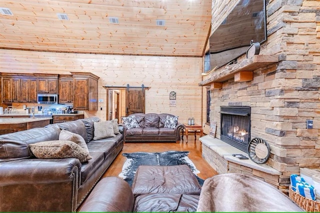 living room featuring light hardwood / wood-style flooring, a barn door, a fireplace, high vaulted ceiling, and wooden walls