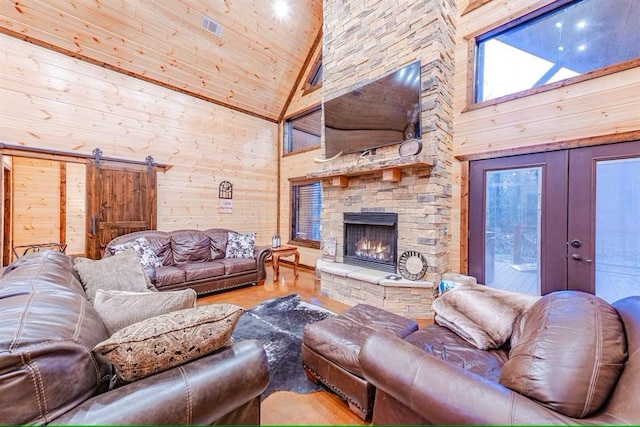 living room featuring a fireplace, french doors, a barn door, wood walls, and high vaulted ceiling