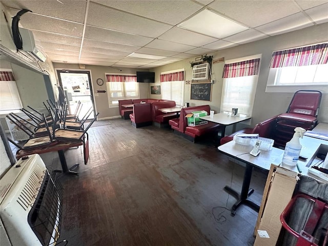 office space featuring a wall mounted AC, hardwood / wood-style floors, a drop ceiling, and a healthy amount of sunlight