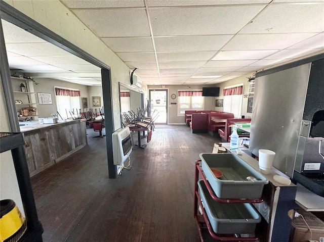 interior space with a drop ceiling, heating unit, and dark hardwood / wood-style floors