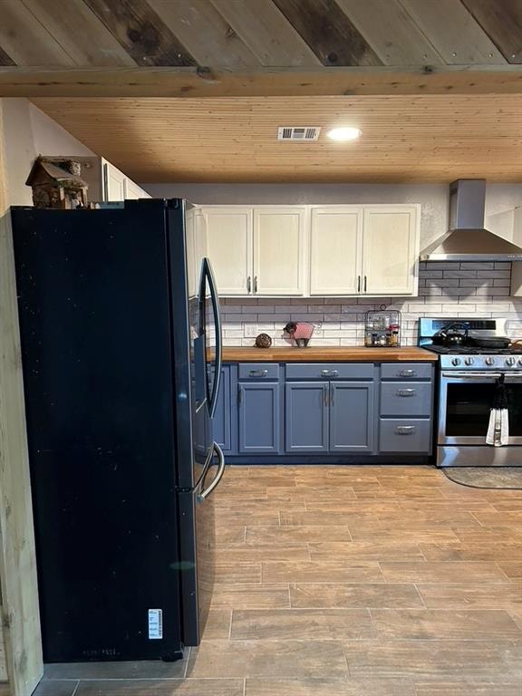 kitchen with stainless steel gas stove, white cabinetry, black refrigerator, and wall chimney range hood