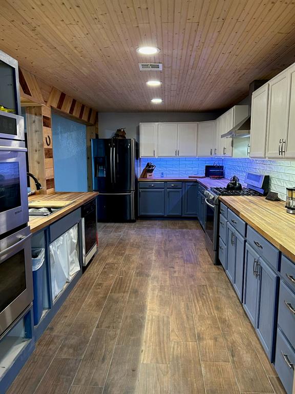 kitchen with wood counters, black fridge, stainless steel gas range, dark hardwood / wood-style flooring, and white cabinetry