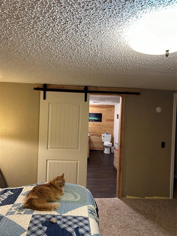 carpeted bedroom with wood walls, a barn door, a textured ceiling, and ensuite bath