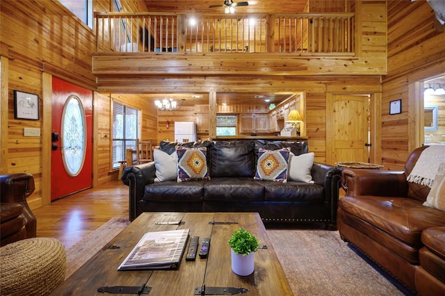 living room featuring wooden walls, hardwood / wood-style flooring, ceiling fan with notable chandelier, and a high ceiling