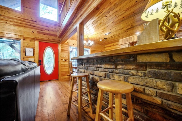 bar featuring a chandelier, hardwood / wood-style floors, wooden walls, and a healthy amount of sunlight